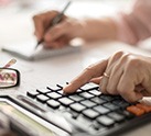 Hand typing on a calculator and writing on a piece of paper in the background